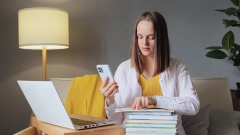 Young woman using smart phone while doing homework for university checking her Stockbeeldmateriaal 254767553