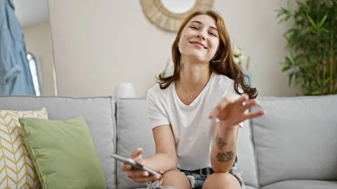 Young woman using smartphone doing ok gesture at home Video stock 247385459