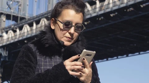 Young woman using smartphone in front of Manhattan bridge from Washington street 스톡 동영상 114577697