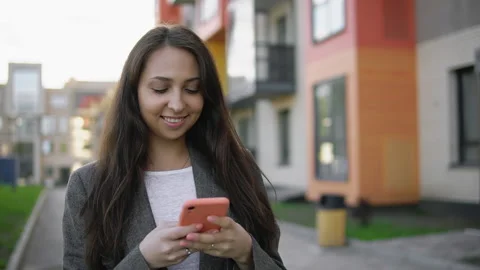 Young woman using smartphone for messaging on urban street at sunset Stock Footage 156468746