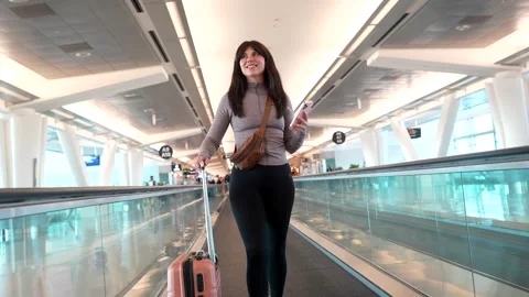 Young woman using smartphone on moving walkway at airport terminal Stock Footage 334540078