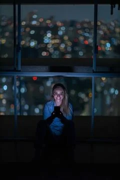 Young woman using a smartphone at night time with city view landscape in the  Stock Photos