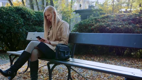 Young woman using smartphone on park bench in autumn daytime Video stock 340739677