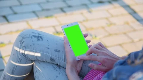 Young Woman using SmartPhone with pre-keyed green screen sitting on the bench 2 Stock Footage 74094532