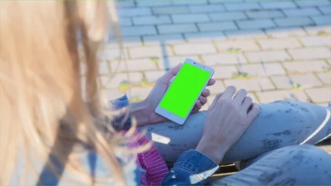 Young Woman using SmartPhone with pre-keyed green screen sitting on the bench 3 Stock Footage 74249703