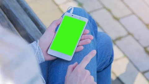 Young Woman using SmartPhone with pre-keyed green screen sitting on the bench 4 Stock Footage 74284570