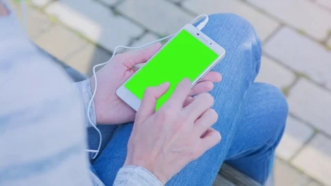 Young Woman using SmartPhone with pre-keyed green screen sitting on the bench 5 Stock Footage 74286111