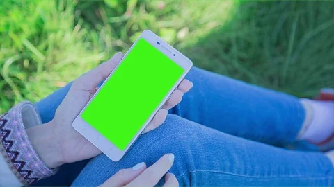 Young Woman using SmartPhone with pre-keyed green screen sitting on the grass 1 Stock Footage 74287355