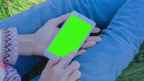 Young Woman using SmartPhone with pre-keyed green screen sitting on the grass Stock Footage 74416306