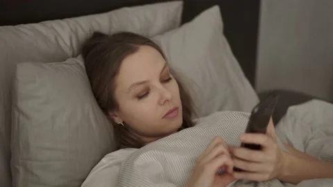 Young woman using a smartphone while lying in bed at home Stock Footage 132049622