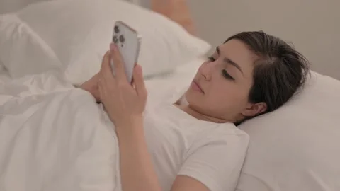Young Woman using Smartphone while Lying in Bed Video stock 238650068