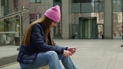 A young woman using smartphone while sitting against a business center. Stock Footage 273015319