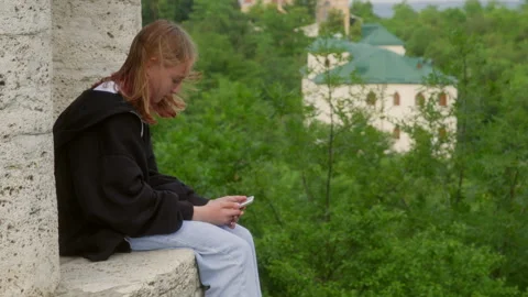 Young woman is using a smartphone while taking a break from exploring a park Stock Footage 291500121