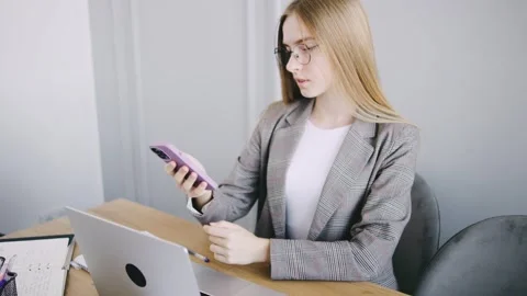 Young woman using smartphone while sitting at a desk in a modern workspace Stock Footage 302658037