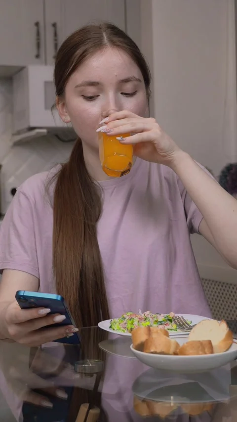 Young woman using smartphone while having breakfast in kitchen 스톡 동영상 311808381