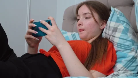 Young woman using smartphone while relaxing on bed Stockbeeldmateriaal 311815075