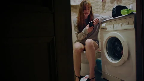 Young woman using smartphone while sitting on toilet Vidéo 332888786