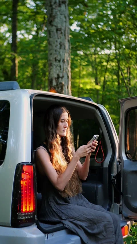 Young woman using smartphone while sitting in open SUV trunk... Video stock 340290974