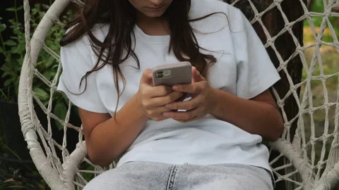 Young Woman Using Smartphone While Relaxing in Hanging Chair Outdoors Stockbeeldmateriaal 345292053
