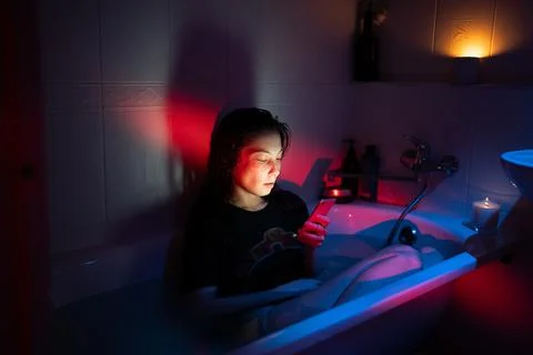Young woman using smartphone while sitting in bathtub full of water, suffering Stock Photos