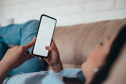 Young woman using smartphone while lying on the couch at home Stock Photos