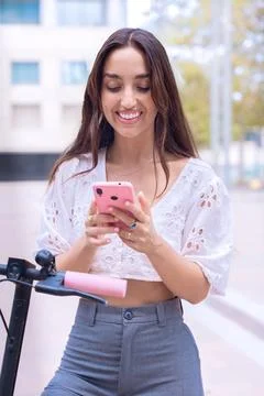 Young woman using smartphone while standing next to an electric scooter.Vertical Stock-Fotos