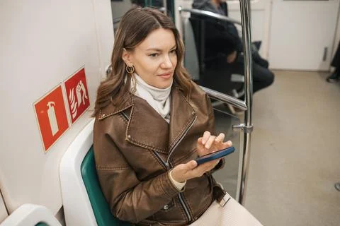 Young Woman Using Smartphone While Sitting on Subway Train in Urban Area During Stock Photos