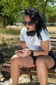Young woman using smartphone while sitting on bench in park with electric s.. Stock Photos