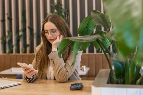 Young woman using smartphone while sitting in cafe with laptop, modern lifestyle 스톡 사진