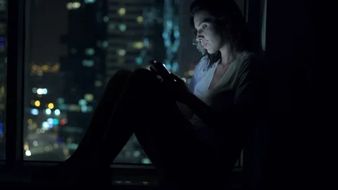 Young woman using smartphone by window during night, 4K Stock Footage 70359250