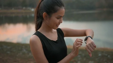 A young woman is using smartwatch while exercise in nature outdoor at sunset Видео 147990320