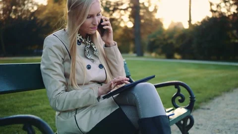 Young woman using tablet and smartphone sitting on park bench outdoors Video stock 340740373