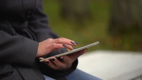 Young woman using tablet computer while sitting on bench in autumn park. Close Stock Footage 82835836