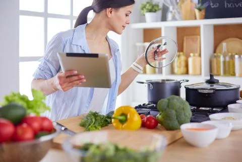 Young woman using a tablet computer to cook in her kitchen. Stock Photos