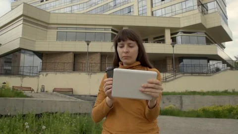 Young woman using a tablet standing on the background of an office building. 스톡 동영상 76937859