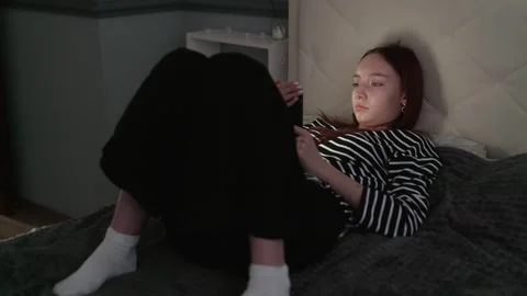 Young woman using tablet while lying on bed in dark bedroom Stock Footage 310925025