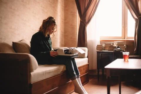 Young woman using typewriter while sitting on sofa at home Stock Photos