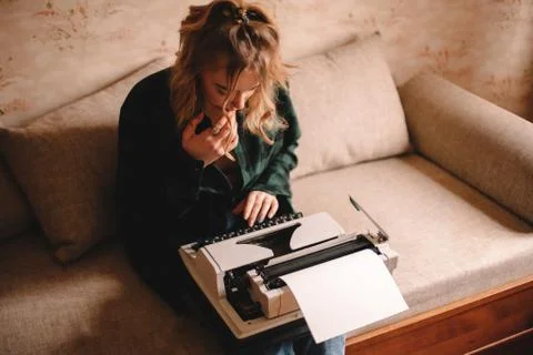 Young woman using typewriter while sitting on sofa at home Stock Photos