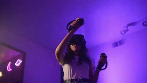 Young woman using VR headset raising controllers in virtual reality interaction Stock Footage 333726085
