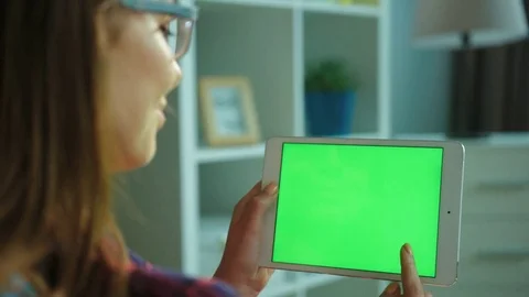 Young woman using white tablet computer with green screen while sitting on the Stock Footage 76355949
