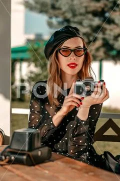 A young woman in a vintage black polka-dot dress with an old camera in her ha Stock Photos