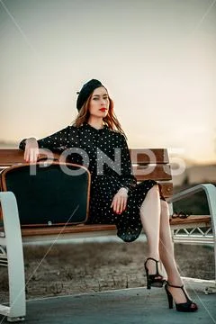 Young woman in vintage black polka dot dress with retro suitcase in hand posi Stock Photos