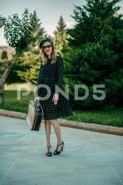 Young woman in vintage black polka dot dress with retro suitcase in hand posi Stock Photos