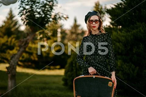 Young woman in vintage black polka dot dress with retro suitcase in hand posi Stock Photos