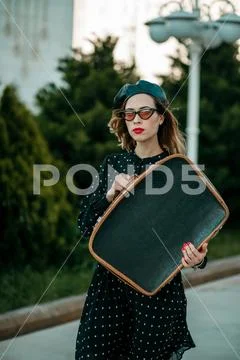 Young woman in vintage black polka dot dress with retro suitcase in hand posi Stock Photos