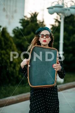 Young woman in vintage black polka dot dress with retro suitcase in hand posi Stock Photos