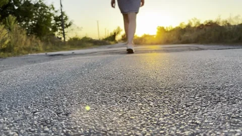Young woman walking along rural road toward glowing sunset. Warm golden light fi Vídeo Stock 342437553