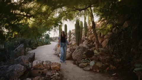 Young woman walking through cactus garden in sunglasses, smiling Stockbeeldmateriaal 335242000