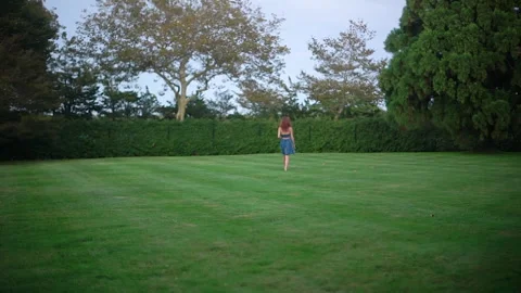 Young Woman Walking Through Empty Green Lawn Under a Cloudy Sky Stock Footage 317648660