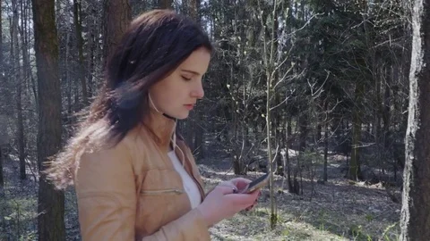 Young woman walking through forestusing and using smartphone Stock Footage 75874952